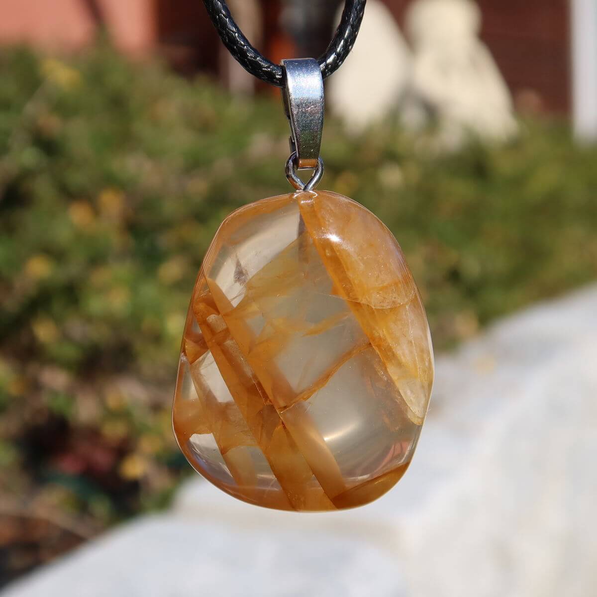 Limonit Quarz Anhänger - Golden Healer - Lebensfreude - Nr. 26, strahlender Quarz mit goldbraunen Einschlüssen vor Naturhintergrund.