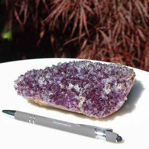 Amethyst Drusen Stück 1A Qualität from Uruguay on display beside a pen, showcasing its unique natural beauty and transformation energy.