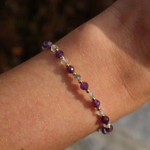 Handmade amethyst and tourmaline quartz faceted gemstone bracelet on wrist, showcasing its vibrant purple and clear stones.