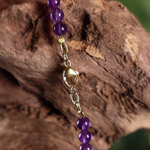Goldener Verschluss der Amethyst Kette mit violetten Perlen auf Holzuntergrund