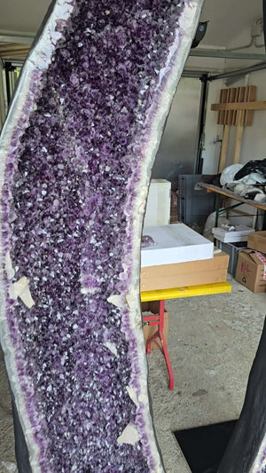 Large amethyst geode displayed upright in a workspace, showcasing deep purple crystals and natural edges