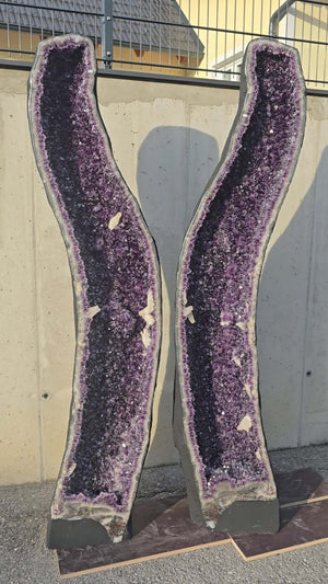 Pair of large AA-quality amethyst geode halves displayed outdoors, showcasing intense dark purple crystals, ideal for luxurious decor.