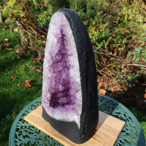 Amethyst Druse geode UNIKAT Nr. 19 with dark AA quality displayed outdoors, enhancing a garden setting with its vibrant violet crystals.