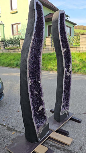 Pair of tall Amethyst geode slices on display stands outside, showcasing deep purple crystals and natural edges