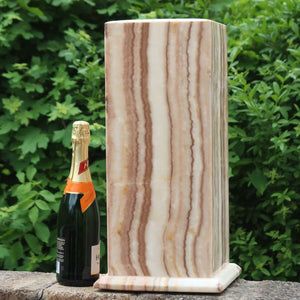 Large Aragonit lamp with LED, handcrafted in Morocco, beside a champagne bottle for scale against a lush green background.