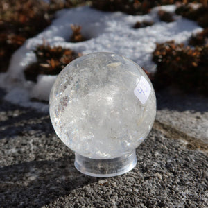 Bergkristall Kugel – Natürliche Kristallkugel 55mm Durchmesser Nr. 43 im Freien auf einem Stein bei winterlichem Hintergrund