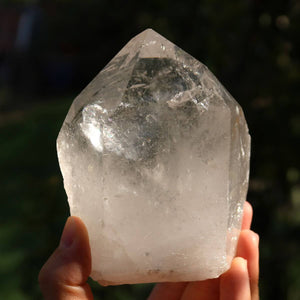 Hand holding a polished quartz crystal point with clear facets, ideal for meditation and clarity, sourced from Brazil.