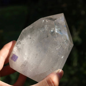 Hand holding a clear Brazilian quartz crystal point with polished facets, enhancing natural sparkle, identified as Unique No. 143.
