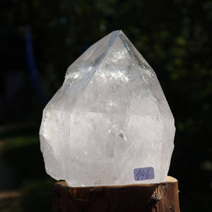 Polished Brazilian clear quartz crystal point for meditation and clarity, shown on a wooden stand. Unique cut shines in sunlight.