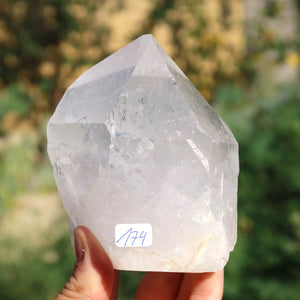 Hand holding Bergkristall Quarz Spitze against a blurred natural background, showcasing its clarity and unique chiseled structure.