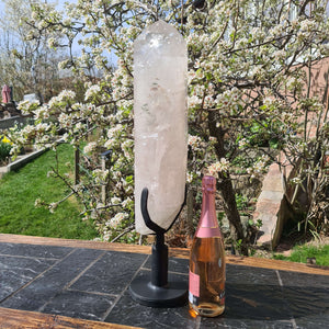 Bergkristall XXL Quarz Spitze auf Metallständer im Freien neben einer Flasche, ideale Raumdekoration für Yoga und Meditation.