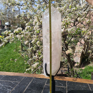 Natürlicher Bergkristall XL auf Metallständer vor blühendem Baum, perfekte Raumdekoration und Meditation, 67 cm hoch, 16,6 kg.