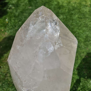 Close-up of a large polished quartz crystal with natural facets, ideal for meditation and home decor on a sunny green background.