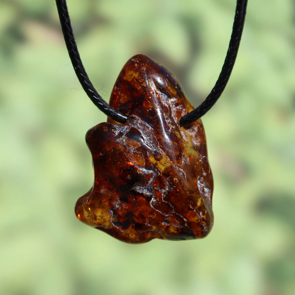Handcrafted 38mm natural amber pendant with unique texture, symbolizing joy and confidence, hanging on a black cord.