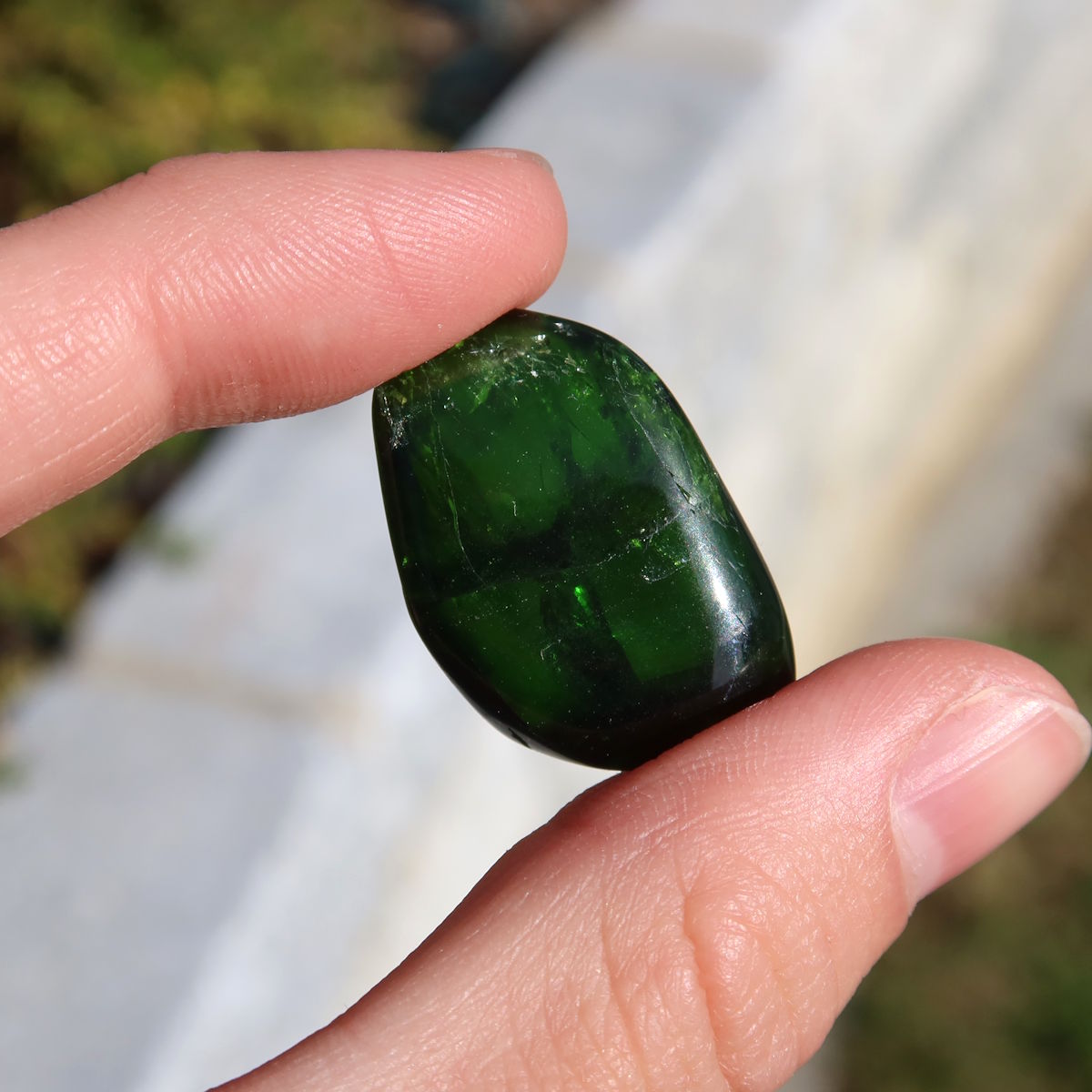 Natürlicher Chromdiopsid Handschmeichler 26mm - Kreativität und Leichtigkeit - UNIKAT Nr. 4 in der Hand gehalten, vor Himmelshintergrund