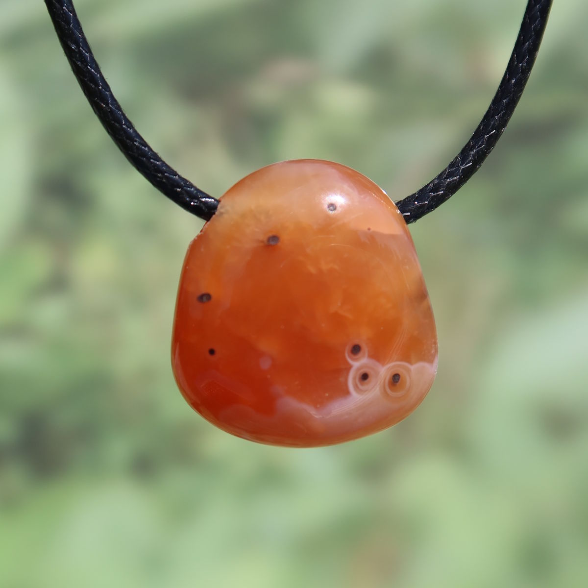 Natürlicher Karneol Anhänger 24mm in leuchtendem Orange, strahlend hängend an schwarzer Kordel; Unikat Nr. 9 für Lebensfreude.
