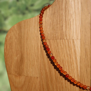Karneol Kette 41cm mit leuchtend orangen und roten Perlen, symbolisiert Selbstbewusstsein und Lebensfreude auf Holzdisplay