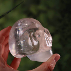 Handcrafted calcite crystal skull in unique shape, 7x7 cm, held against a blurred green background, exquisite gemstone decor.