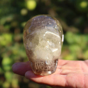 Handcrafted citrine crystal skull, 10x7 cm, unique gemstone art piece displayed outdoors on a person's palm.