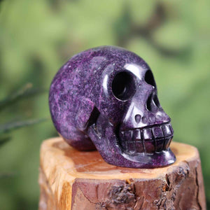 Handmade crystal skull from natural stone on wooden stand, unique design with purple hues, size 7x6 cm.