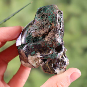 Handcrafted Uvarovite Garnet Crystal Skull, unique collectible with intricate detailing, held against a green background.