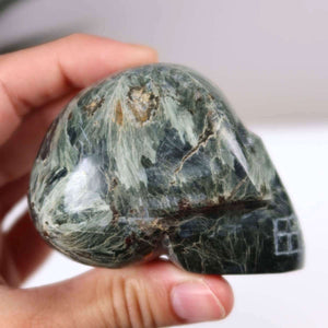 Handcrafted Seraphinite crystal skull in unique shape, perfect for collectors, shown in hand for size reference.