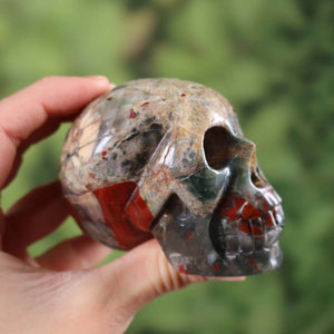 Handcrafted volcanic jasper crystal skull in unique shape, 7x5 cm, collector's item in a person's hand.