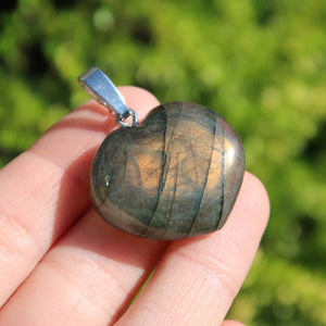 Heart-shaped labradorite pendant held in hand, showcasing vibrant blue, green, and gold hues under sunlight.