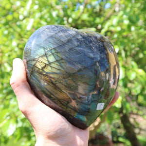 Hand holding a large labradorite heart stone with iridescent colors, ideal for relaxation and enhancing creativity, unique piece.
