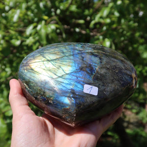 Hand holding a large Labradorite heart stone with iridescent blue and green hues, unique Unikat Nr. 1 against a natural background.