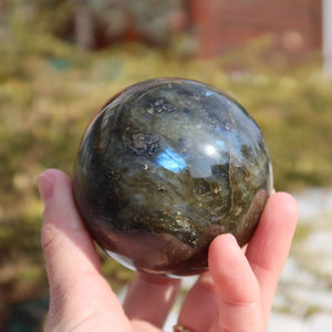 Hand holding a polished Labradorite sphere with shimmering colors, perfect for home decor, available for online purchase at Steinwelten.