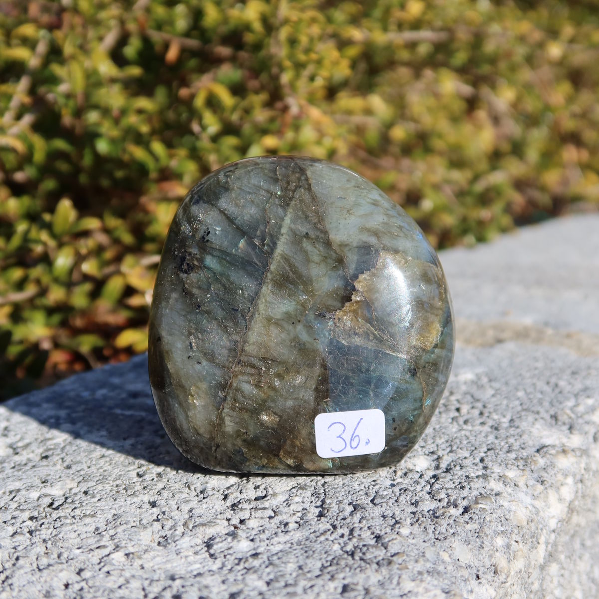 Labradorit Freiform poliert - 6x6cm - Intuition und Kreativität Nr.36 auf grauem Stein mit natürlichem Hintergrund.