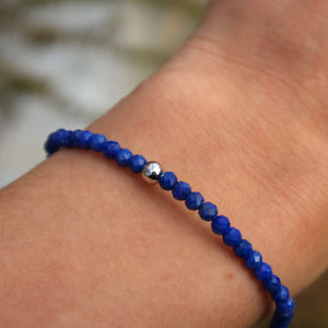 Hand wearing a handmade lapislazuli bracelet with faceted beads and Herkimer diamond, featuring deep blue gemstones.