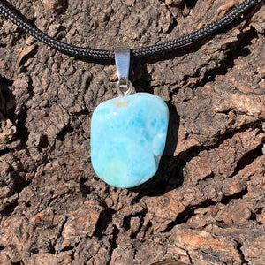 Larimar pendant with silver bail, unique gemstone from the Dominican Republic, set against a textured dark background.