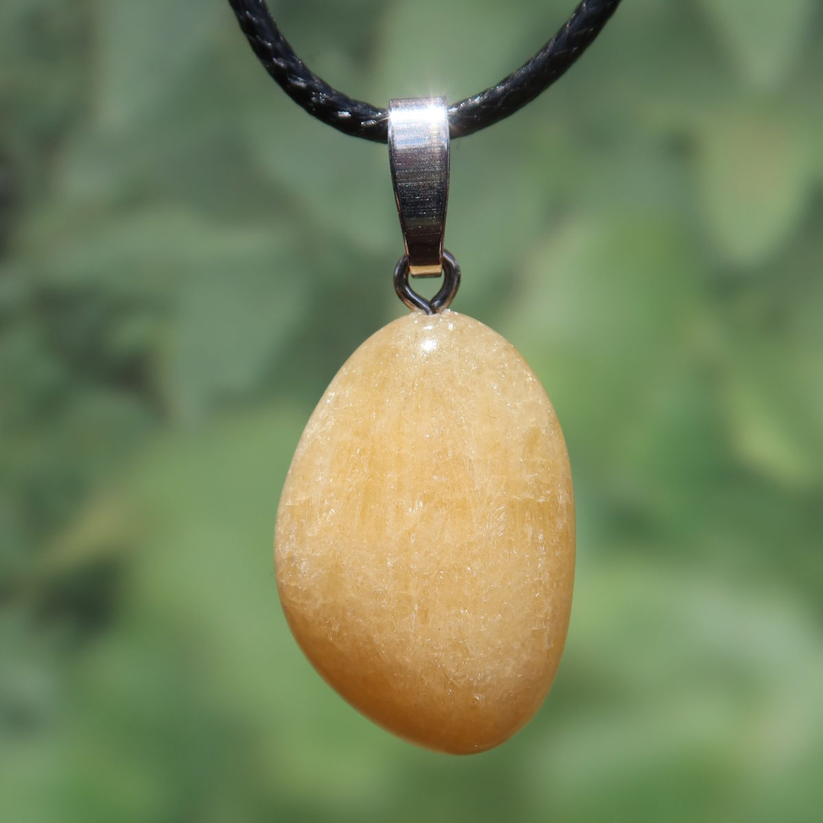 Calcit orange Anhänger - Selbstvertrauen und Positivität - Nr. 20, strahlend und warm auf schwarzem Halsband.