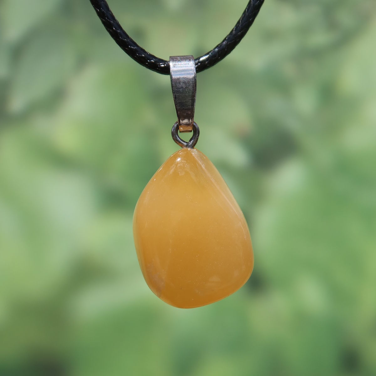 Calcit orange Anhänger - Selbstvertrauen und Positivität - Nr. 28 auf einem schwarzen Halsband mit grüner Hintergrund.