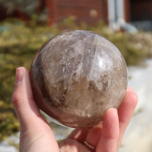 Hand holding polished smoky quartz sphere, highlighting its unique deep brown and gray tones. Available online at Steinwelten.