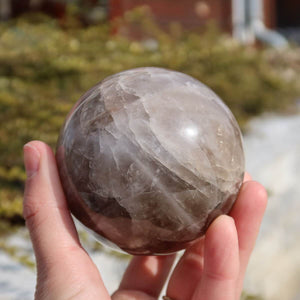 Hand holding Rauchquarz Kugel, a polished smoky quartz sphere with deep brown hues, available at Steinwelten Graz and Wiener Neustadt.