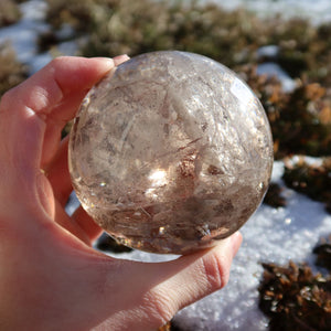 Rauchquarz Kugel – Natürliche Kristallkugel 80mm Durchmesser Nr. 46 in Sonnenlicht, zeigt rauchig braune Töne und glatte Oberfläche.