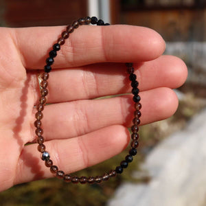 Hand holding a handmade faceted smokey quartz and black tourmaline gemstone bracelet, 17cm long, in daylight.