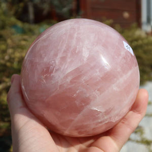 Hand holding a polished rose quartz sphere, unique item No. 11, showcasing its soft pink hue and clear structure. Available at Steinwelten online.