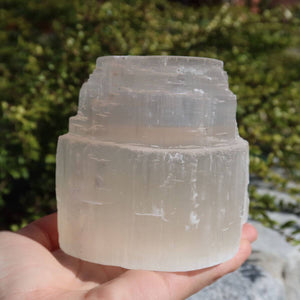 Hand holding a natural selenite crystal tealight holder outdoors.