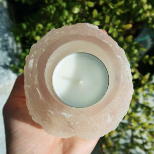 Hand holding a natural Selenite crystal tealight holder, 8cm, known for stress relief and protection, outdoors with greenery background.