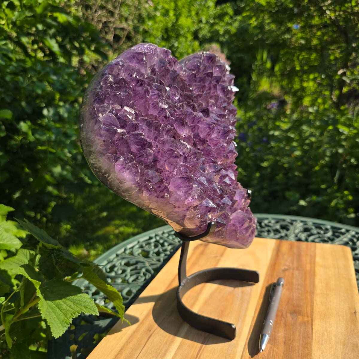 Amethyst Druse Amethyst Geode in Herzform mit Metallsockel 31x28x12cm - NR-24 auf einem Tisch im Freien.