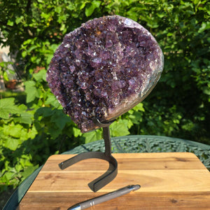 Amethyst Druse Amethyst Geode in Herzform mit Metallsockel 33x28x15cm - NR-16 auf einem Tisch im Freien.