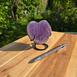 Amethyst Druse Amethyst Geode in Herzform mit Metallsockel 10x9x7cm - NR-55 auf einem Holztisch mit Stift