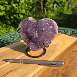 Amethyst Druse Amethyst Geode in Herzform mit Metallsockel 11x11x9cm - NR-47 auf einem Holztisch mit Stift