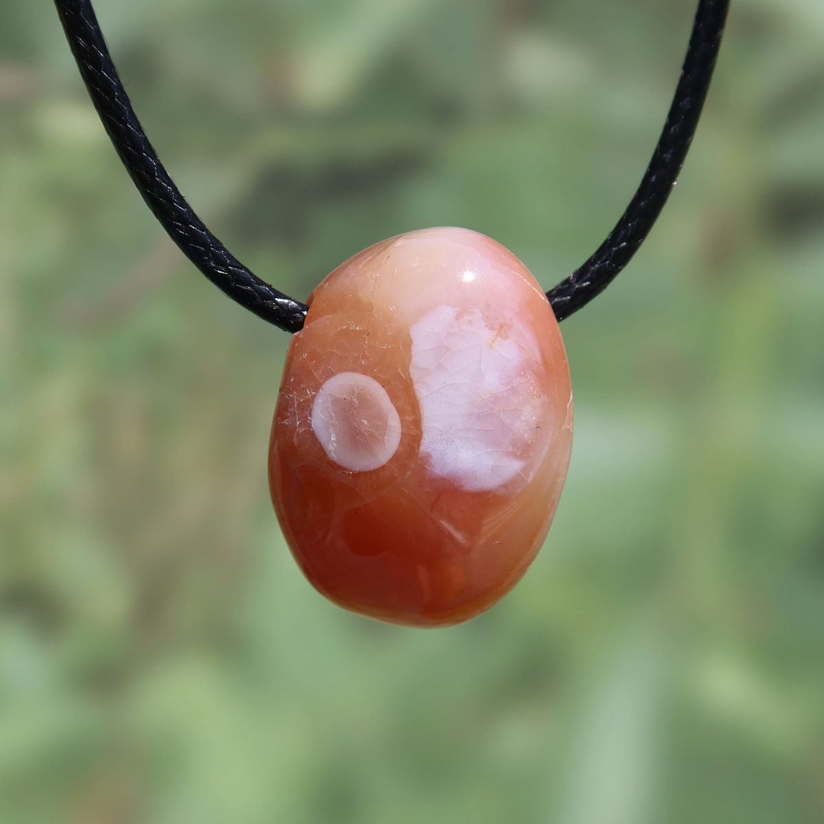 Karneol Anhänger auf schwarzem Band, natürliche Maserungen, leuchtendes Orange-Rot, einzigartiges Design, steigert Lebensfreude und Energie.