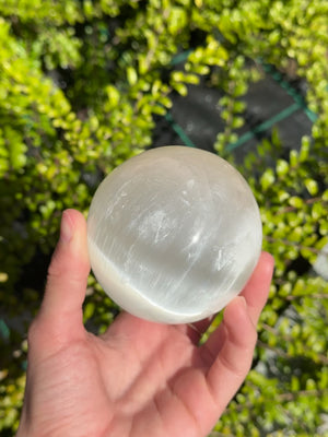 Hand holding Natürliche Selenit Kristall Kugel 80mm (Marienglas, Gips) - Lichtbringer und Schutzstein outdoors.