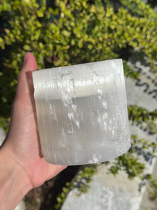 Hand holding a translucent 8cm selenite tealight holder against greenery background, known for its calming and protective properties.